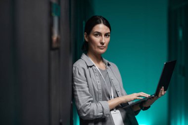 Dizüstü bilgisayar tutan kadın veri mühendisinin belden yukarı portresi ve sunucu odasında süper bilgisayarla çalışırken kameraya bakmak, boşluğu kopyalamak