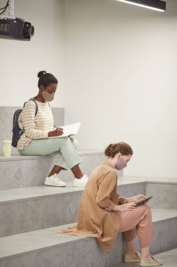 Modern salonda çalışırken okulda maske takan iki genç kadının dikey yan görüntüsü.