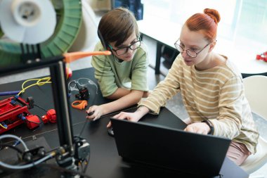 High angle view at young female teacher helping boy using 3D printer during robotics and engineering class at school