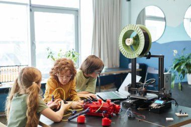 Group of children building robot and using 3D printer during engineering class at school, copy space