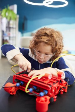 Vertical portrait of cute boy building robot during engineering class in development school