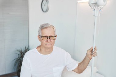 Hastane odasındaki son sınıf öğrencisinin belden yukarı portresi seruma tutunup kameraya bakıyor, boşluğu kopyalıyor.