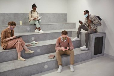 Modern okul salonunda sosyal mesafeli rahatlarken maske takan çeşitli öğrenci gruplarına geniş açılı bakış açısı