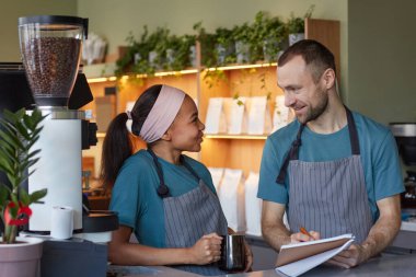 Waist up portrait of two young baristas smiling while enjoying work in cafe or coffee shop, copy space