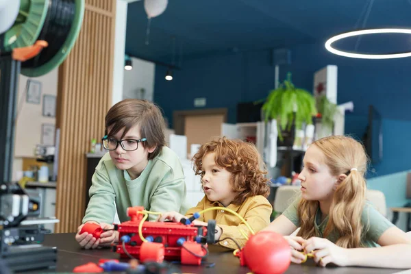 Portrait of three children operating robots during engineering class at modern school, copy space