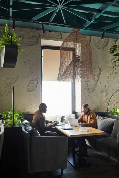 在绿色阁楼室内阳光照射下 在咖啡厅桌上工作时使用笔记本电脑的两个同时代男人的垂直宽角度肖像 复制空间 — 图库照片