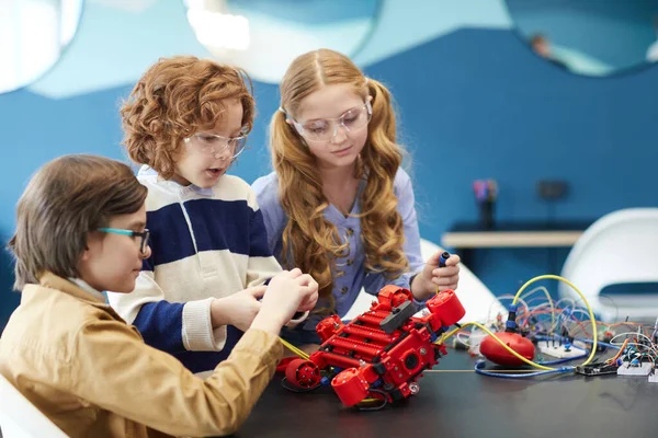 Portrait of three cute children building robot together while enjoying engineering class in development school