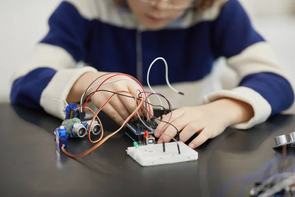 Close up of unrecognizable child experimenting with electric circuits while building robots during engineering class in school