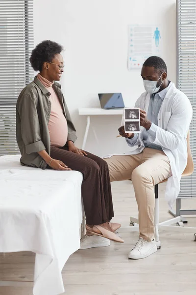 African doctor examining the ultrasound image and talking to pregnant woman at hospital he prescribing treatment for her