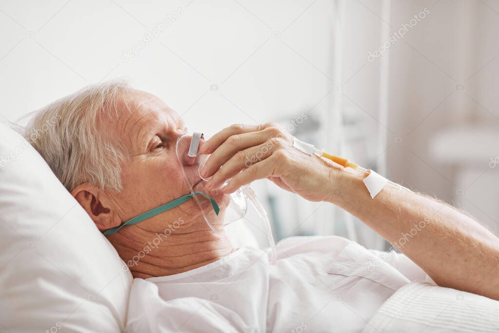 Side view portrait of sick senior man lying in hospital bed with oxygen supplementation mask and IV , copy space