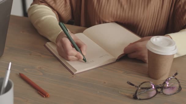 机の上に紙コップと眼鏡をかけ ペンでノートに書き込み 切り取られた認識できない人のロックダウン — ストック動画