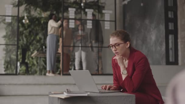 中等比例的专业白人女性坐在办公室与现代室内环境 在手提电脑上打字 看着站在后台的同事 — 图库视频影像