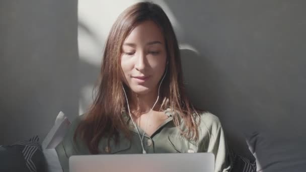 여성의 이어폰을 실내에 이야기하고 노트북 컴퓨터를 사용하여 비디오 — 비디오