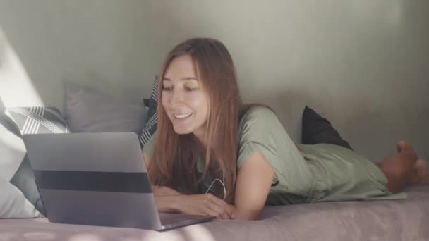 全景照片 白种人快乐女人头戴耳机 躺在沙发上 枕头装饰 用笔记本电脑上网 — 图库视频影像