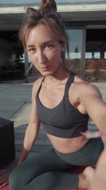 Spor kıyafetleri giymiş, terasta oturmuş, gülümseyen ve selfie kamerasında konuşan neşeli beyaz kadınların el bilgisayarı POV 'u.