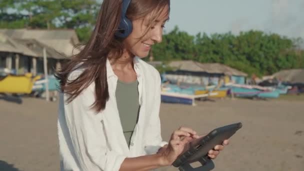 헤드폰을 타블렛 컴퓨터를 사용하고 말하고 다리가 해변에 여성의 사진을 있었습니다 — 비디오