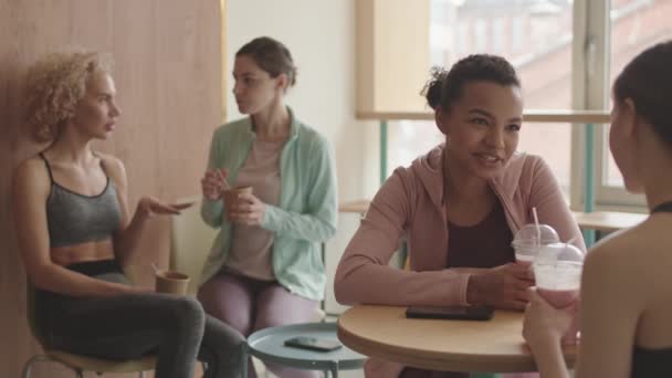 年轻漂亮的混血女子的胸部用吸管用塑料杯喝冰沙 与不认识的人交谈 两个女性朋友在运动后在后台吃零食 — 图库视频影像