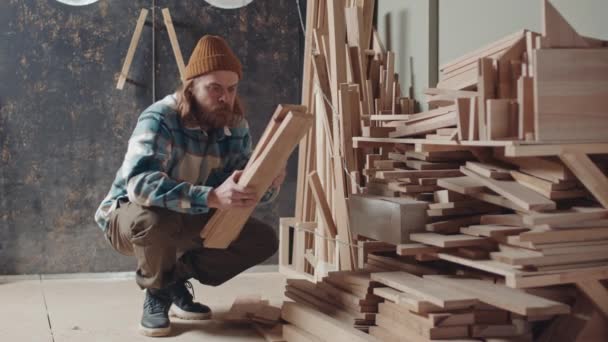 男の髭を生やした白人大工の腕に腰を下ろし 木の板を選んで仕事をし 家を出る — ストック動画