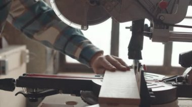 Tahta kesmek için otomatik testere kullanan, kareli gömlek giyen, tanınmayan erkek marangozun yakınına.