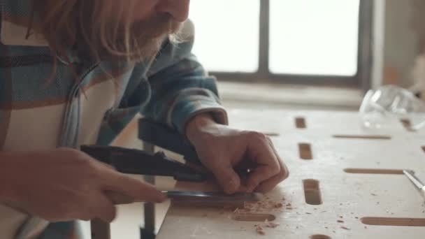穿着格子衬衫 留着胡子的白人男性木匠站在精雕细琢车间的工作台旁 用雕刻刀雕刻木片 — 图库视频影像