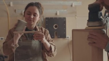 Beyaz adamın çalışma masasında durup el yapımı ahşap kutuyu zımparalarken kadınların zımpara kağıdı kullanarak el zımparalama makinesini kullanması.