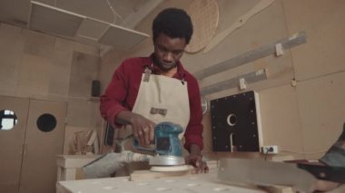 Genç Afrikalı işçinin, doğrama atölyesinde el değirmeni makinesiyle çalışırken orta boy fotoğrafı.
