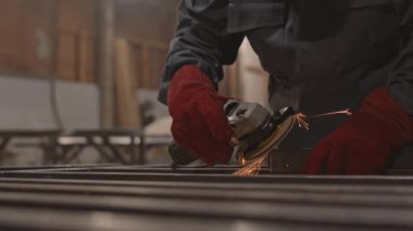 İşçi ceketi ve kırmızı eldivenler giyen, küçük kare metalik borularda zımpara kullanan, tanınmayan kişilerin yakın çekimleri.