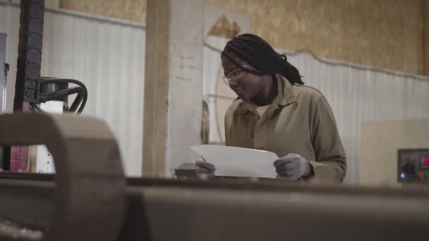 Die Junge Afrikanische Mechanikerin Trägt Schutzbrille Und Handschuhe Hält Papier — Stockvideo