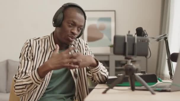 中镜头中 年轻的非洲裔美国说唱歌手身穿耳机坐在家里 一边在智能手机摄像机上录音一边说唱 — 图库视频影像