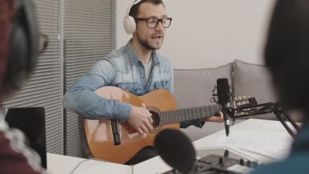 在广播节目中 年轻的中年白人男性音乐家头戴耳机弹奏吉他和唱歌的背景图 — 图库视频影像