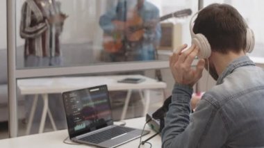 Müzik grubu yeni albüm kaydediyorken, erkek beyaz ses mühendisinin stüdyoda m-audio keystation ve laptop üzerinde çalışmasının arka görüntüsü