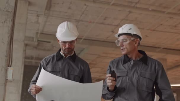 Kamerafahrt Von Zwei Kaukasischen Arbeitern Gespräch Die Arbeiterjacken Harthüte Und — Stockvideo