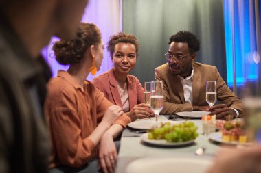 Bir grup genç arkadaşla yemek yerken masada sohbet ediyorlar.