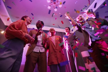 İçerideki arkadaşlarla parti yaparken konfeti banyosu altında duran çeşitli gençlerin düşük açılı görüntüsü