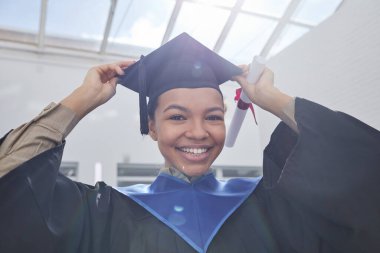 Mezuniyet şapkası takan ve gün ışığında kameraya gülümseyen Afro-Amerikalı genç bir kadının düşük açılı portresi.