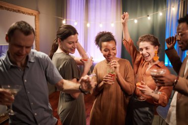 Waist up view at multi-ethnic group of friends enjoying party indoors and dancing together cheerfully