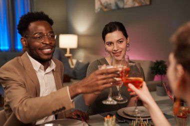 Portrait of elegant mixed-race couple enjoying dinner with friends indoors and toasting over festive table