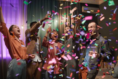 Diverse group of excited young people dancing under confetti shower while enjoying party with friends indoors clipart