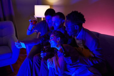 Farklı arkadaş grupları, mavi ışıklarla aydınlatılan kapalı hava partisinde selfie ya da görüntülü sohbet yapıyorlar.