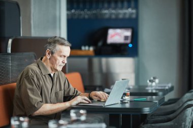 Masada oturup laptopla kafede çalışan, bıyıklı, son sınıf beyaz adam.