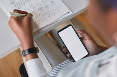 Yüksek açı, okulda matematik sınavına girerken elinde boş ekranla akıllı telefon tutan, sınav konseptinde kopya çeken tanınmamış Afro-Amerikan öğrencinin yüksek açılı yakın çekimi.