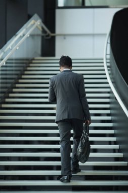Genç Afro-Amerikalı iş adamının ofis binasında merdivenlerden yukarı çıkışına uzun uzun bakıyorum.