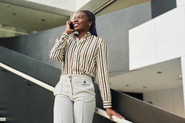 Ofiste akıllı telefondan konuşan gülümseyen Afro-Amerikalı iş kadınının düşük açılı portresi, boşluğu kopyala