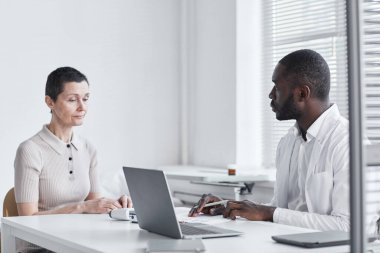 Afrikalı doktor, doktorun muayenehanesi sırasında masada oturup hastayla konuşuyor.