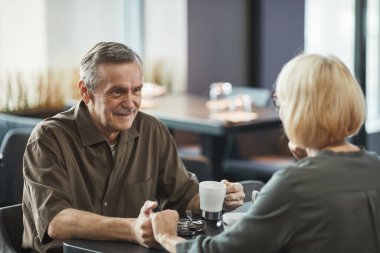 Gülümseyen, bıyıklı, çay içen ve kafede sohbet ederken sevgili bir kadının elini tutan son sınıf öğrencisi.