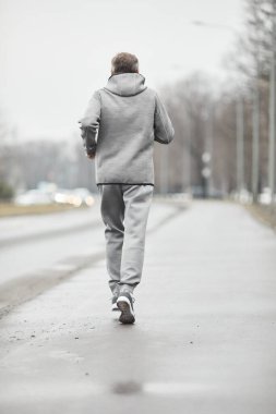 Soğuk sonbaharda tek başına antrenman yaparken yolda koşan gri takım elbiseli, sportif yaşlı bir adam.