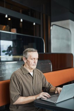 Odaklanmış, bıyıklı, modern kafede oturan ve taşınabilir bilgisayarla ilgili rapor hazırlayan beyaz bir adam.