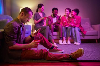 İçerideki partide yerde otururken akıllı telefon kullanan genç bir adamın yan görünümü