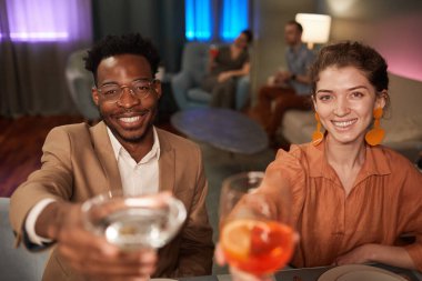 Zarif bir melez çiftin portresi arkadaşlarıyla akşam yemeğinin tadını çıkarıyor ve kameraya kadeh kaldırıyor.