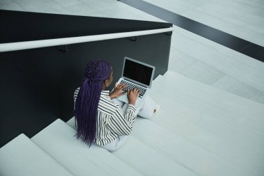 Ofisteki merdivenlerde otururken dizüstü bilgisayar kullanan Afro-Amerikalı iş kadınının grafiksel arka görüntüsü, boşluğu kopyala